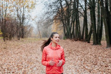 Güzel sonbahar şehir parkında renkli sonbahar yapraklarıyla koşan genç bir kadın.