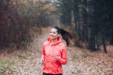 Koşucu, sonbahar parkı arka planında bulutlu bir günde koşuyor.