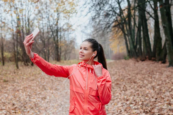 Uzun siyah saçlı güzel fitness kızı selfie çekiyor ve kulaklıkla müzik dinliyor. — Stok fotoğraf