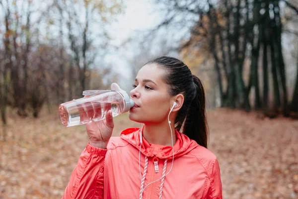 Junge Sportlerin trinkt frisches Wasser aus der Flasche im Herbstpark. Sportlicher Lebensstil. — Stockfoto