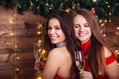 Mutlu Noeller ve mutlu yıllar. Kırmızı elbiseli iki mutlu kadın şampanya içip Noel 'i kutluyorlar.