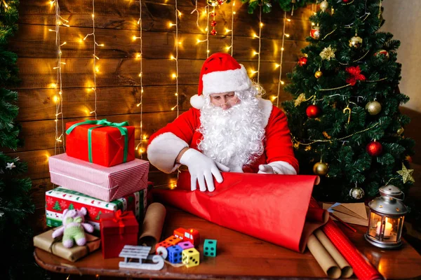 God jul och god jul. Santa Clause förbereder presenter till barn för Xmas vid skrivbord hemma. — Stockfoto