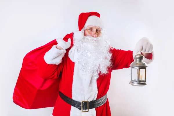 Santa Claus carrying big red bag full of gifts and light the road on white background. — Stockfoto