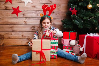 Mutlu küçük kız evde Noel ağacının yanında hediyelerle oturuyor.