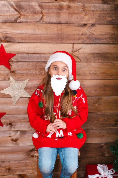 Linda niña en el sombrero de Santa sentado en el fondo de madera —  Fotos de Stock