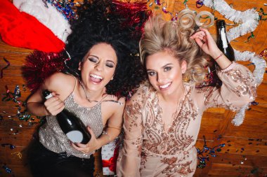 Parti eğlencesi. Dans eden, şampanya içen ve yerde yatan iki güzel genç kadın.