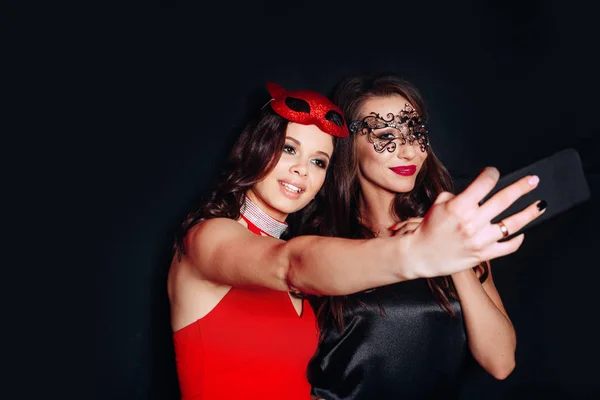 Duas jovens mulheres de festa sorrindo tirando foto selfie no celular sobre fundo preto — Fotografia de Stock