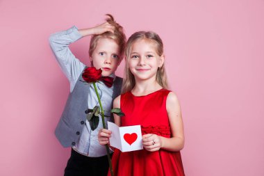 Elinde sevgililer günü kartı olan altı yaşında tatlı bir kız ve pembe arka planda komik bir çocuk.