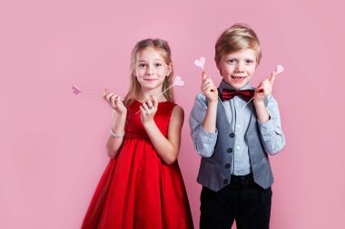 Pembe arka planda kırmızı kalpler taşıyan küçük kız ve erkek çocuk portresi.