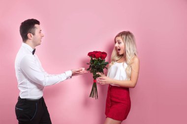 Yakışıklı bir adam pembe arka planda güzel bir kadına evlenme teklif ediyor.