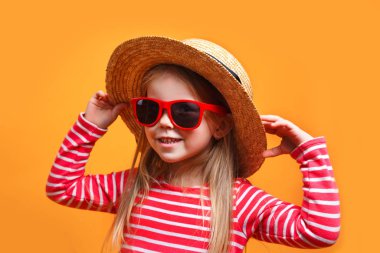 Cute little girl wearing a hat and sunglasses on yellow background