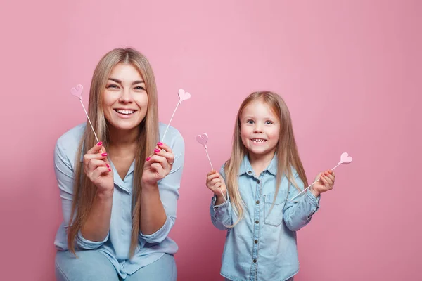 Lovely girl funny playing with her smiling mom on pink background — 스톡 사진