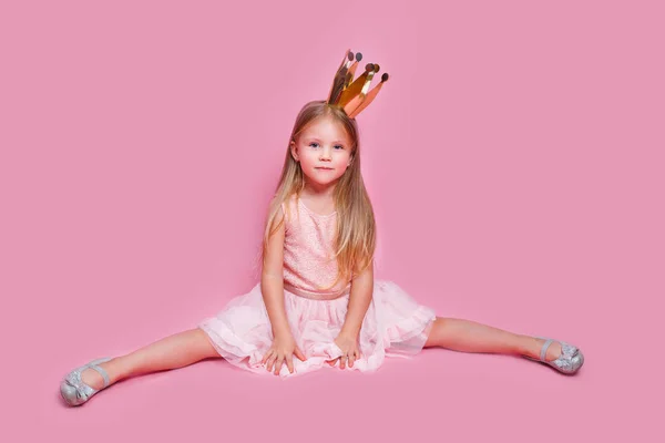 Little girl sitting on a twine in pink princess dress and crown on pink background