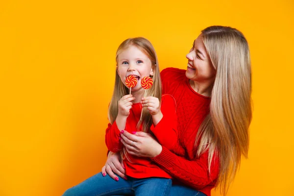 Daughter and mother eat sweet candies on yellow background. Mothers Day — 스톡 사진