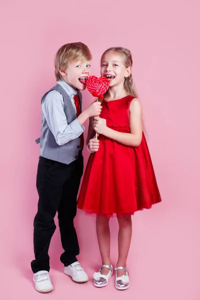 Funny boy and little girl with candy red lollipop in heart shape. Beautiful children eat sweets. Valentines day — 스톡 사진