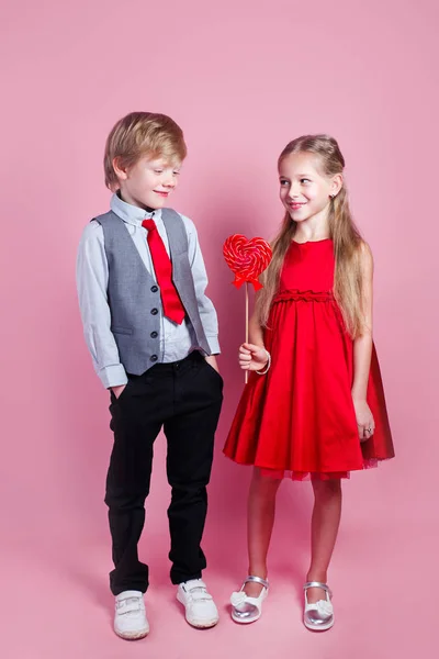 Vicces fiú és kislány, cukorka piros nyalókával a szívükben. A gyönyörű gyerekek édességet esznek. Valentin-nap — Stock Fotó
