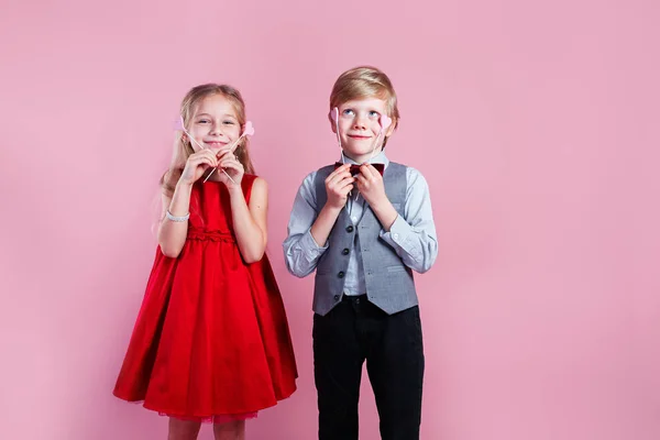 Portrait of cute little boy and girl holding red hearts on pink background — 스톡 사진