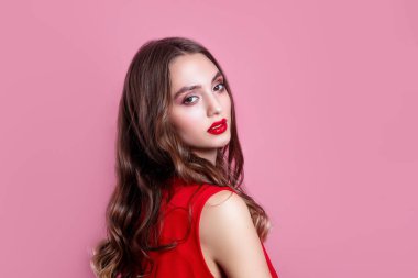 Kırmızı dudaklı, makyajlı ve pembe arka planda kırmızı elbiseli güzel bir kadın.