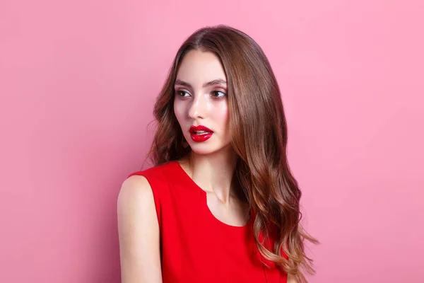 Mladá krásná hezká žena s dlouhými kudrnatými vlasy a rudými rty v červených šatech dívá pryč — Stock fotografie