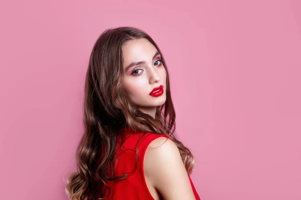 Bella donna con labbra rosse, trucco e acconciatura in abito rosso su sfondo rosa — Foto Stock