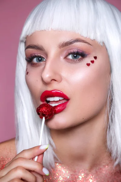 Beauty Glamour model woman with trendy white hair style and creative makeup holding red sweet lollipop candy