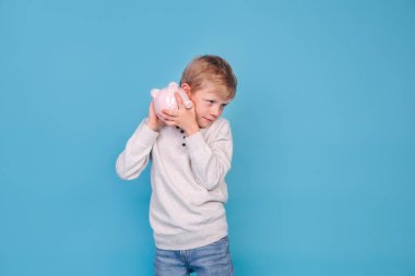 Sevimli küçük çocuk mavi arka planda domuz kutusunu sallıyor.