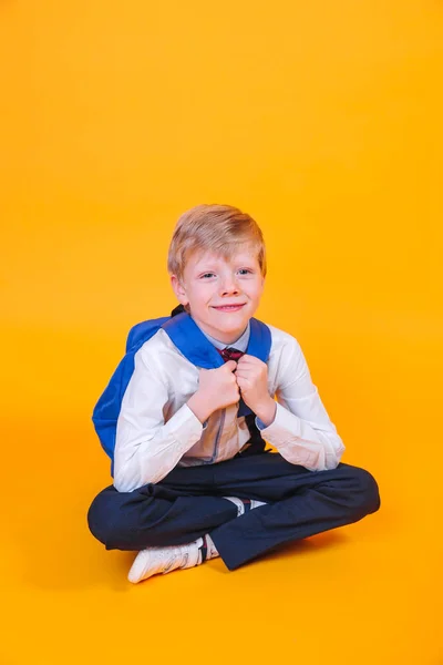 Маленький школьник с рюкзаком сидит на оранжевом фоне — стоковое фото
