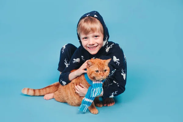 Kid in zachte warme pyjama spelen met rode kat op gele achtergrond — Stockfoto