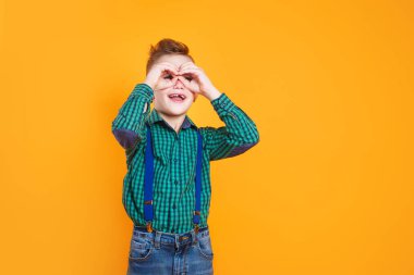 Küçük çocuk gülümsüyor. Elleri gözlerinde, parmaklarının arasından bakıyor.