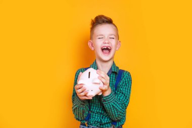 Sarı arka planda kumbarası olan heyecanlı küçük çocuk.