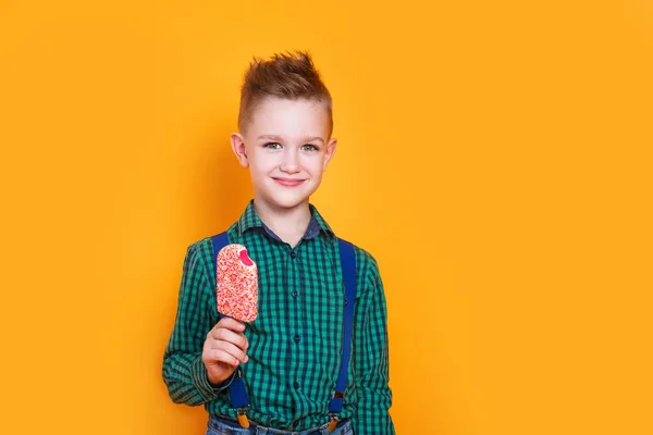 Мальчик ест клубничное мороженое и смеется на желтом фоне. — стоковое фото