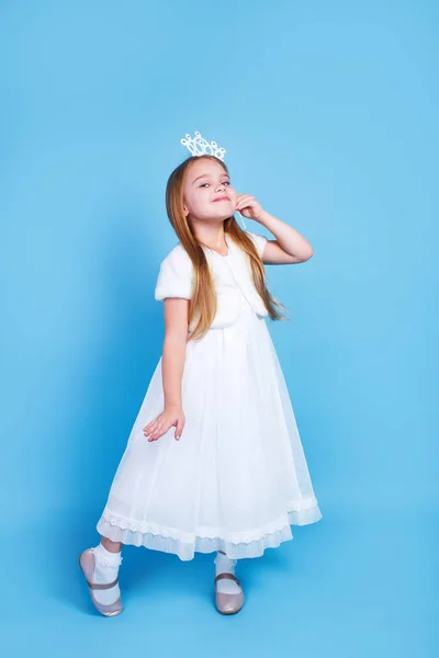 Linda niña con el pelo largo en vestido blanco que sostiene la corona de princesa en la cabeza sobre fondo azul . — Foto de Stock