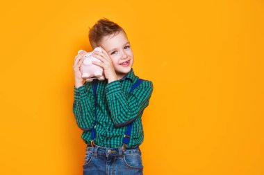 Cute little boy shaking moneybox on orange background