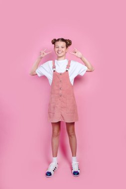 Beyaz tişörtlü, pembe kotlu, boynuzlu ve kameraya bakan güzel bir kız.