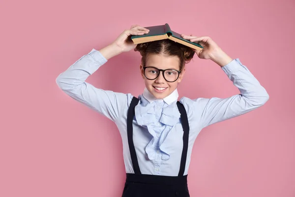 안경을 쓰고 학교 유니폼을 입고 책을 머리에 쓰고 있는 웃긴 소녀 — 스톡 사진