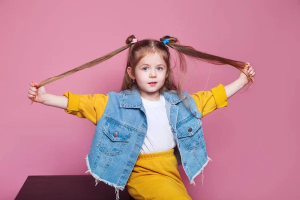 Милая маленькая девочка вытягивает волосы на розовом фоне — стоковое фото