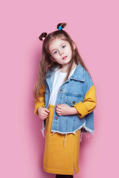 Милая маленькая девочка-модель в джинсах на розовом фоне. Концепция моды — стоковое фото
