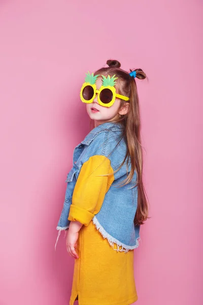 Модная маленькая девочка в больших солнцезащитных очках ананаса позирует на розовом фоне — стоковое фото