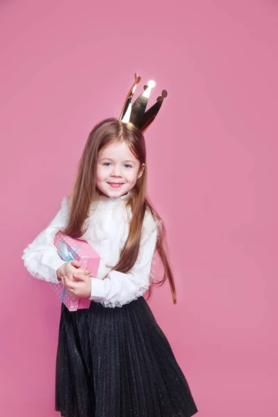 Happy little girl in crown holding birthday present box on pink background — Φωτογραφία Αρχείου