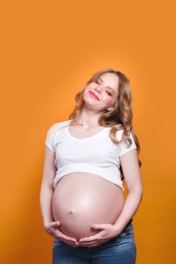Pregnant happy woman with close eyes touching her belly on yellow background
