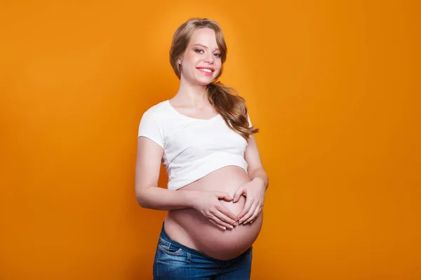 Pregnant woman holding her hands in a heart shape on her pregnant belly with fingers heart symbol. — Stockfoto
