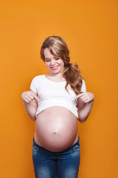 Studio shot of pregnant woman wearing white T-shirt pointing to her stomach — Stockfoto