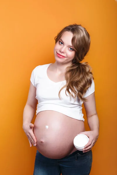 Pregnant woman applying cream on her belly on yellow background — Stockfoto