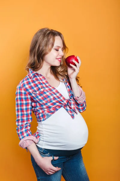 Beautiful pregnant woman eating apple on yellow background — Stockfoto