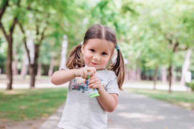 Şirin küçük kız parkta sabun köpüğü üflüyor.