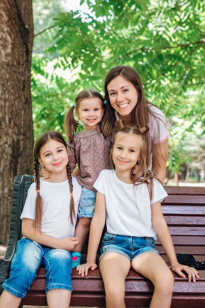Happy family mother and three child daughters sitting and laughing in park — Stock Photo, Image