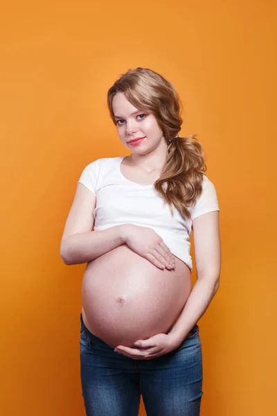 Gravid lycklig kvinna röra sin mage på gul bakgrund — Stockfoto