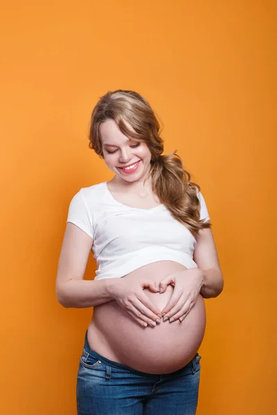 Pregnant woman holding her hands in a heart shape on her pregnant belly with fingers heart symbol. — Stockfoto