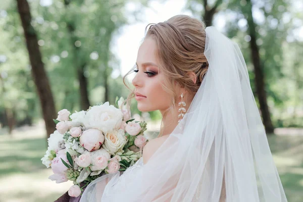 Krásná nevěsta se svatební květiny bouque v parku. Nevěsta se svatební make-up a účes. — Stock fotografie