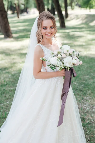 Impresionante novia joven celebración de ramo de boda y sonriendo a la cámara al aire libre — Foto de Stock